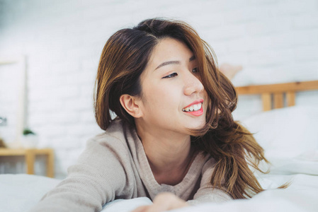 肖像美丽的年轻亚洲妇女在床上的早晨在家里。愉快的亚洲妇女穿着舒适的毛衣和微笑在她的床上。放松的房间。生活方式亚洲妇女在家庭概念