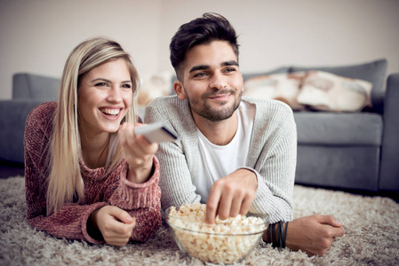 幸福的夫妇看电视和在家里吃爆米花