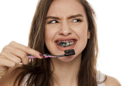 年轻妇女刷牙用黑色的牙齿糊与活性炭在白色背景