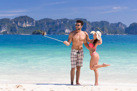 青年夫妇采取自拍照照片海边夏天度假海滩，蓝色的水