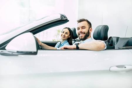 快乐的年轻夫妇坐在新的白色汽车经销商, 侧面视图