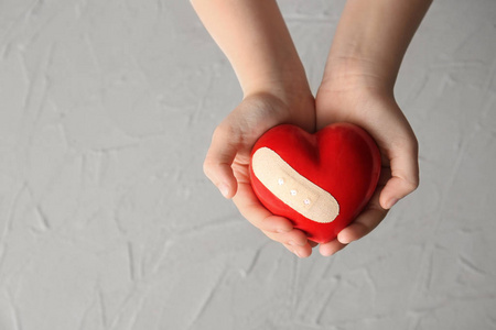 手的孩子持有红色的心脏与石膏在光的背景。医疗保健理念