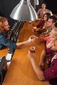 年轻人在酒吧，酒保朋友坐在木制柜台酒吧，喝啤酒集团