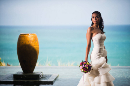 新娘穿着奢华的白色连衣裙, 摆出一条对大海的姿态