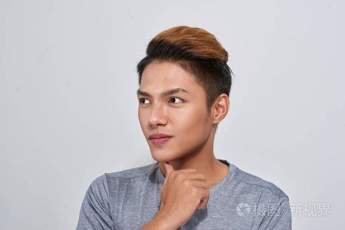 英俊年轻的微笑沉思的男子站在灰色背景上仰望
