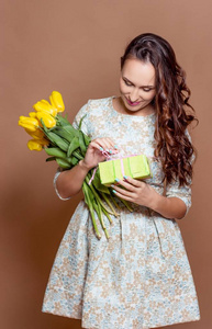 年轻漂亮的女人抱着一束黄色的郁金香和礼品盒。春天