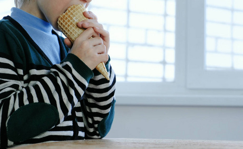 不认出的男孩在条纹夹克吃冰淇淋在垫铁在家