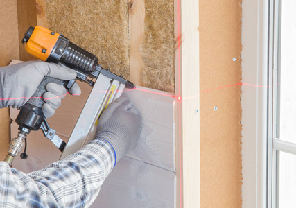 工人用一层白色木板完成墙面的抛光工作, 使用激光线水平。用木纤维板材建筑隔热生态木框架房屋