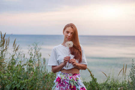 快乐美丽的女人吹蒲公英的天空和海洋背景, 有乐趣和玩户外, 享受自然, 暑假和假期, 年轻漂亮的女子捧花, 愿望概念