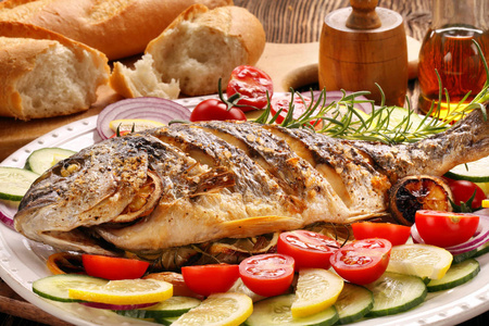 烤的鱼, 法棍面包和蔬菜在盘子上照片