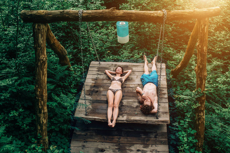 夏天露营。年轻夫妇躺在木秋千上, 日光浴, 放松。家庭, 青年, 温泉自然概念