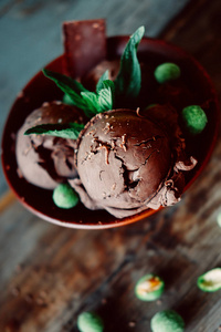 三勺黑可可冰淇淋圣代与薄荷叶和辛辣涂满绿色花生的巧克力洒在一起