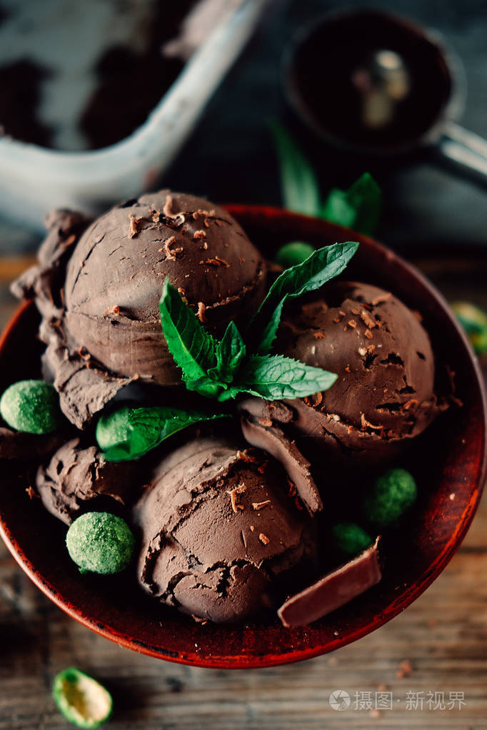 三勺黑可可冰淇淋圣代与薄荷叶和辛辣涂满绿色花生的巧克力洒在一起