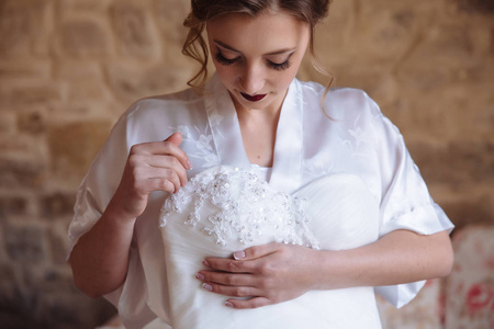 一个卷发和长睫毛的女孩看着她的婚纱, 她握着她的手。新娘欣赏她婚纱的刺绣图案和布料。