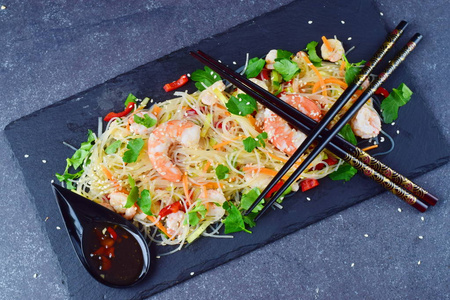 虾与黑石板灰色抽象背景上的传统东方酱蔬菜面条。健康食品的概念