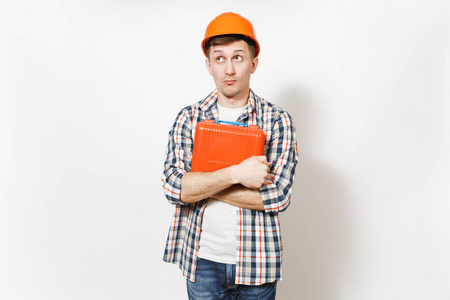 年轻好奇英俊的男子在保护性橙色安全帽持有案件与仪器或工具箱隔离在白色背景。设备, 翻新公寓房间的工具。修复主页概念