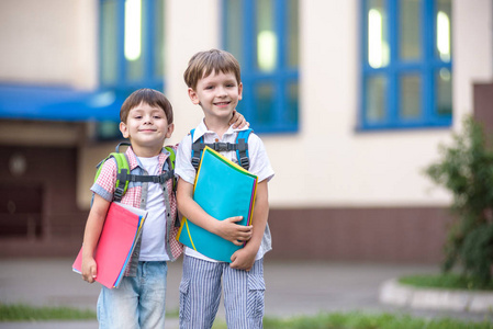 可爱小学校学生轻快地谈校园。孩子们有个好心情。温暖的春天的早晨。后面在同学书包的肩。在手中的男孩明亮的文件夹之一