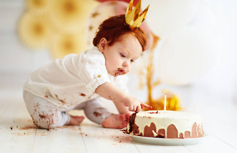 好奇的搞笑宝宝男孩的手指戳在他第一次的生日蛋糕