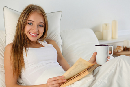 年轻美丽微笑的金发女子躺在床上看书老博