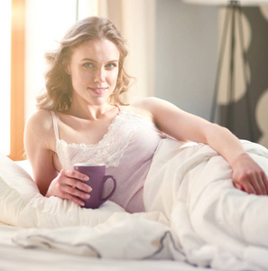 年轻女子躺在床上喝杯咖啡或茶图片