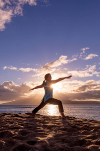 一个女人在日落时分在毛伊岛的海滩上练瑜伽