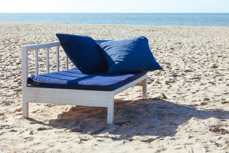 美丽的海滩上有两个蓝色的垫子在贵妃休息室。清晨的阳光照亮了大海和沙子的土堆