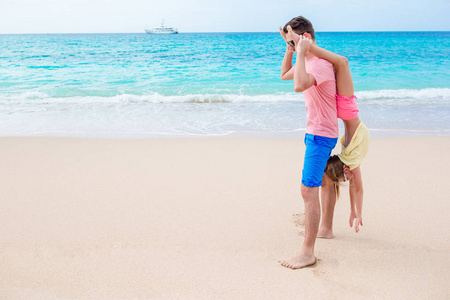 父亲和运动的小女孩的家庭在海滩上玩得开心