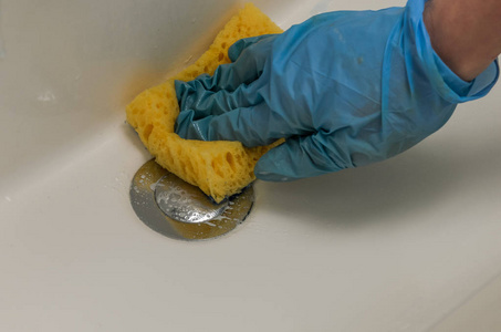 一个戴手套的女人在浴室里用抹布洗水管工和水龙头, 还有家用化学品。