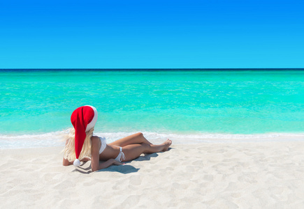 圣诞圣诞老人的帽子在热带海洋海滩晒日光浴的女人