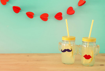 新鲜柠檬水饮料的形象在可爱的仙人掌形状的眼镜戴着胡子和嘴唇, 在木桌和心花环背景。热带夏日浪漫假期概念
