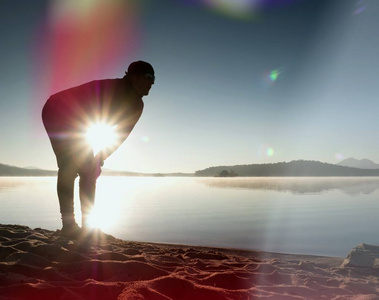 积极的人行使和日出时在湖滩上伸展的剪影