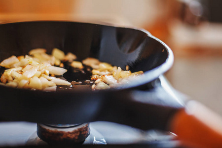 在老铸铁锅中煮熟的植物油煎炸过程中的白洋葱和蒜片