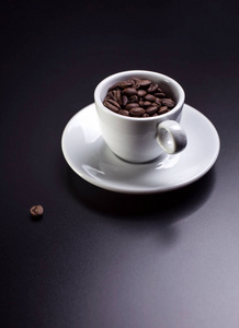 白色杯子与咖啡豆在黑暗的桌背景, 垂直的射击