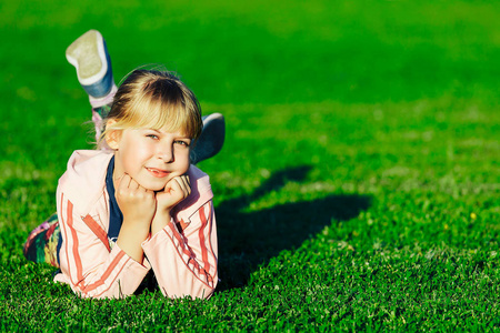 金发的小女孩躺在绿色的草地上开阔的天空下，看着镜头