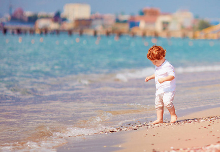 可爱的红发学步的婴儿漫步在夏日沙滩上