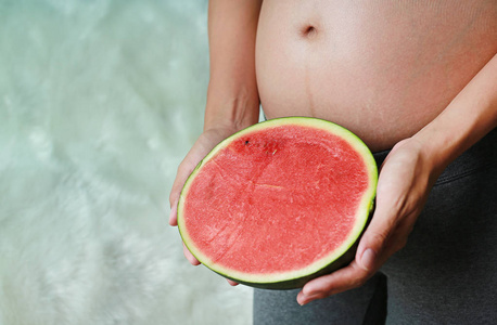 怀孕妇女坐和举行切开半西瓜在她的腹部