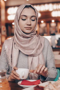 美丽的年轻阿拉伯妇女与头巾在她的头上用餐在一个舒适的美丽的咖啡馆