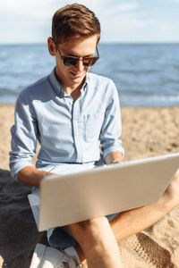 戴眼镜的年轻人, 在沙滩上的笔记本电脑上工作, 度假