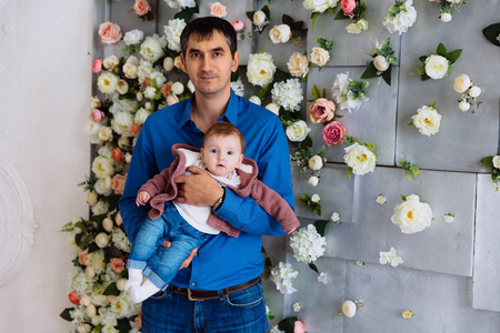 一个男人抱着他的小女儿。父亲抱着一个婴儿在他的怀里用花的墙