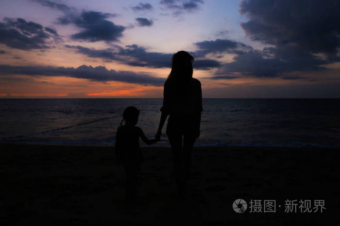 日落背景下与海边小女孩漫步的女性人物黑色剪影