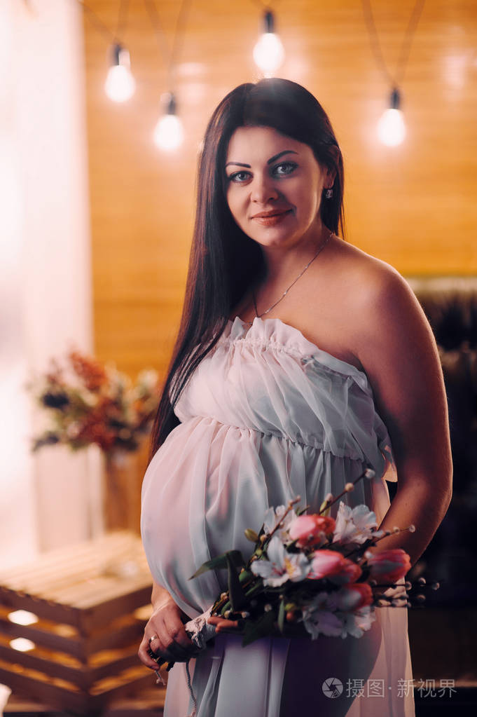 孕妇在件漂亮的白色衣服摸她的肚子用手和抱着一束牡丹的特写图像一个