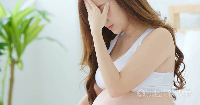 怀孕的妇女坐在床上感到抑郁在家中