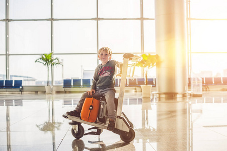 可爱的小男孩与橙色行李箱在机场。在男孩上手推车和机场