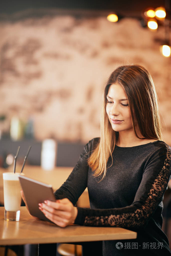 年轻的白种女人坐在咖啡馆喝咖啡时使用片剂