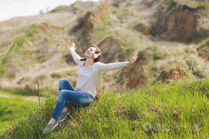 年轻的微笑轻松美丽的女人与闭上眼睛的轻休闲服装与耳机听音乐坐在