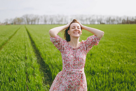 年轻的微笑轻松漂亮的女人与闭上眼睛的光图案的衣服抱着头走在阳光