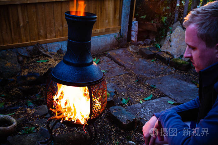 年轻男子坐在露天火在黄昏.由露营火的人的穆迪照片.一个体贴的年轻人