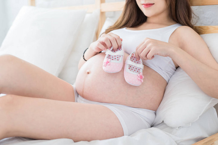 怀孕妇女抱着小婴儿鞋在床上