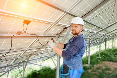 独立太阳能光电面板系统的安装和布线。在太阳能电池组件内的硬帽连接电缆中, 年轻电工的特写。替代能源概念