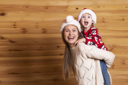 一个美丽的母亲与一个小女儿在圣诞老人的帽子看观众和微笑